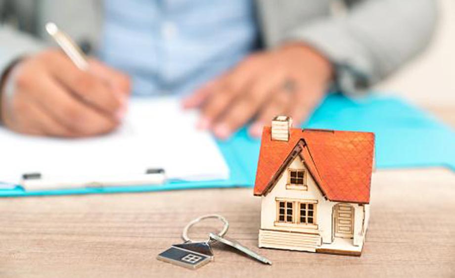Man filling out paperwork with mini house and keys in front